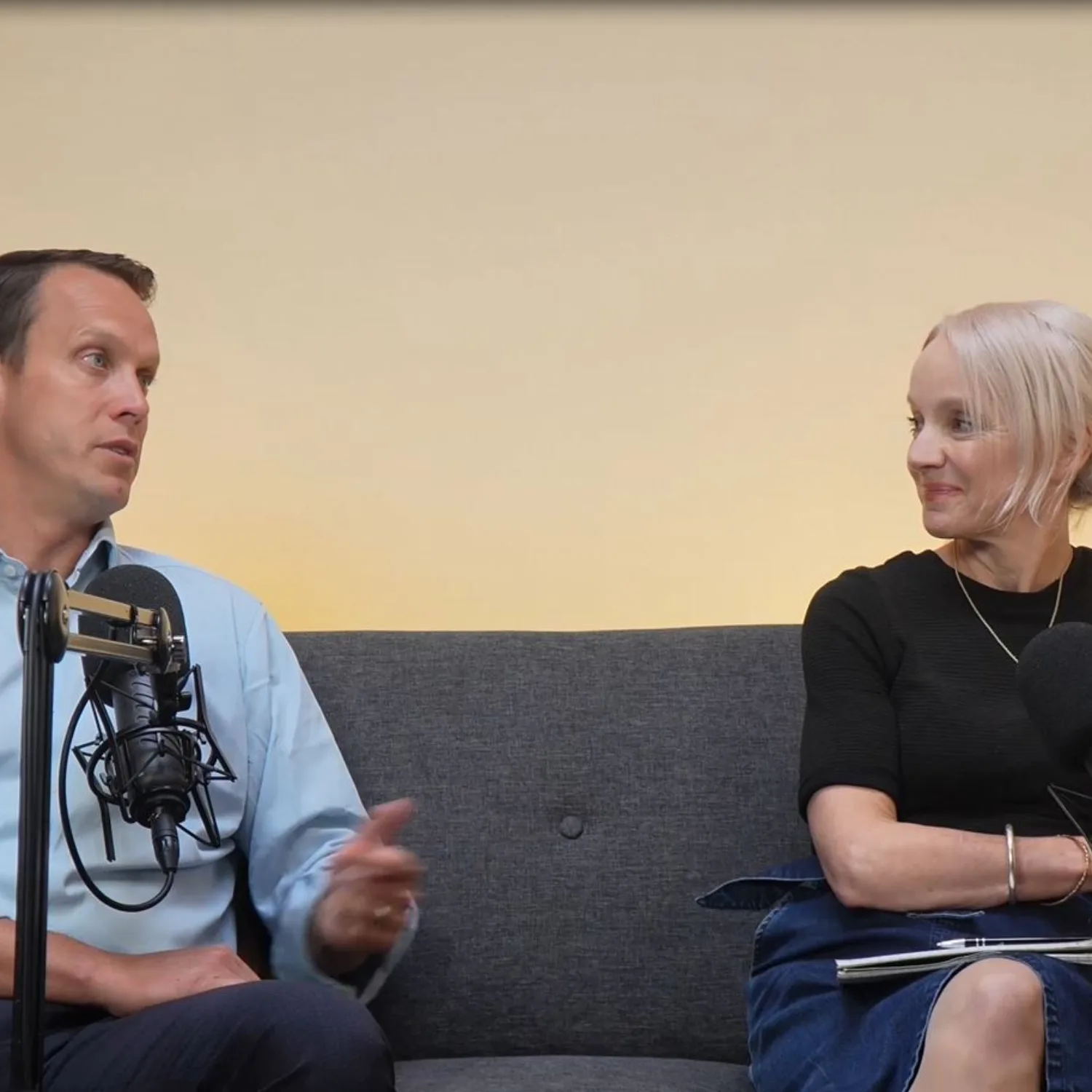 Robin Pritchett and Anna Hollyman sitting on grey sofa talking into microphones